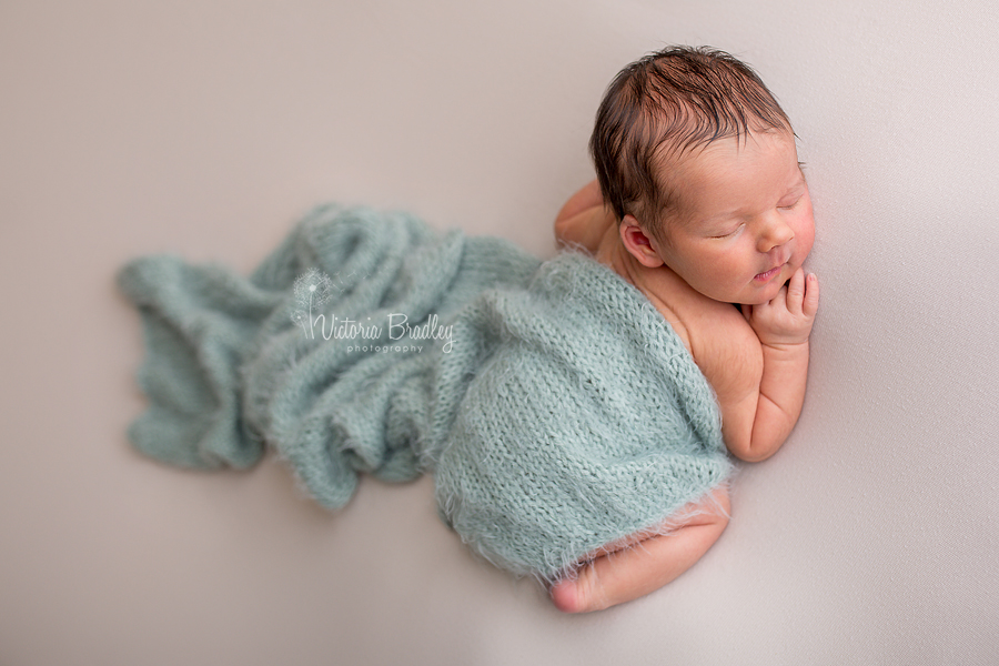 newborn baby boy on cream backdrop with pale sage wrap