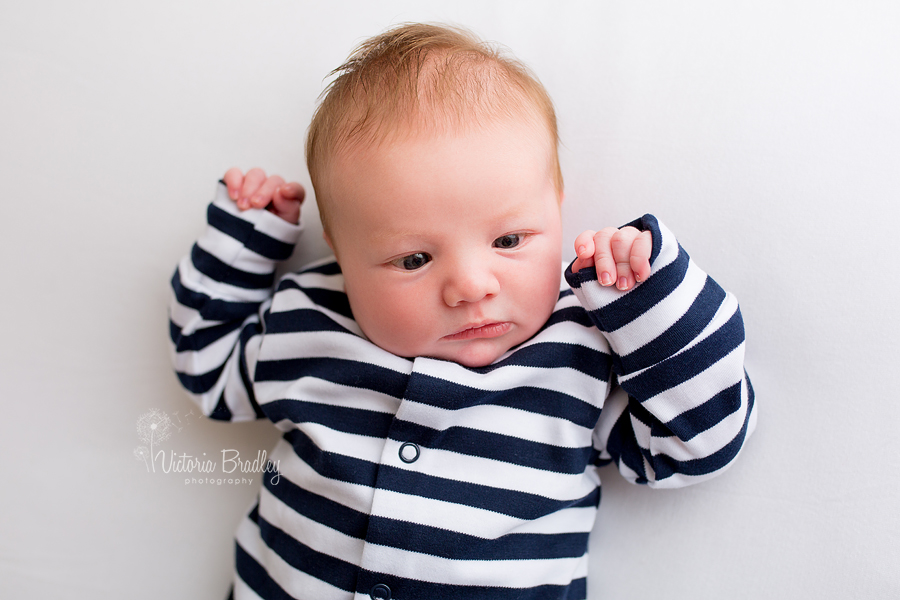 newborn boy is striped sleep suit on white backdrop, newborn photography