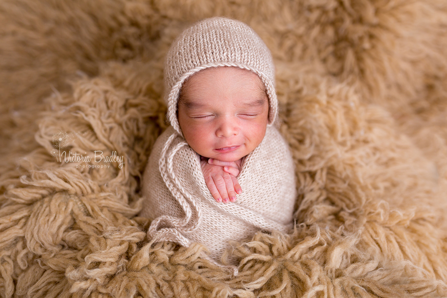 Smiley newborn in potato sack pose on caramel flokati rug