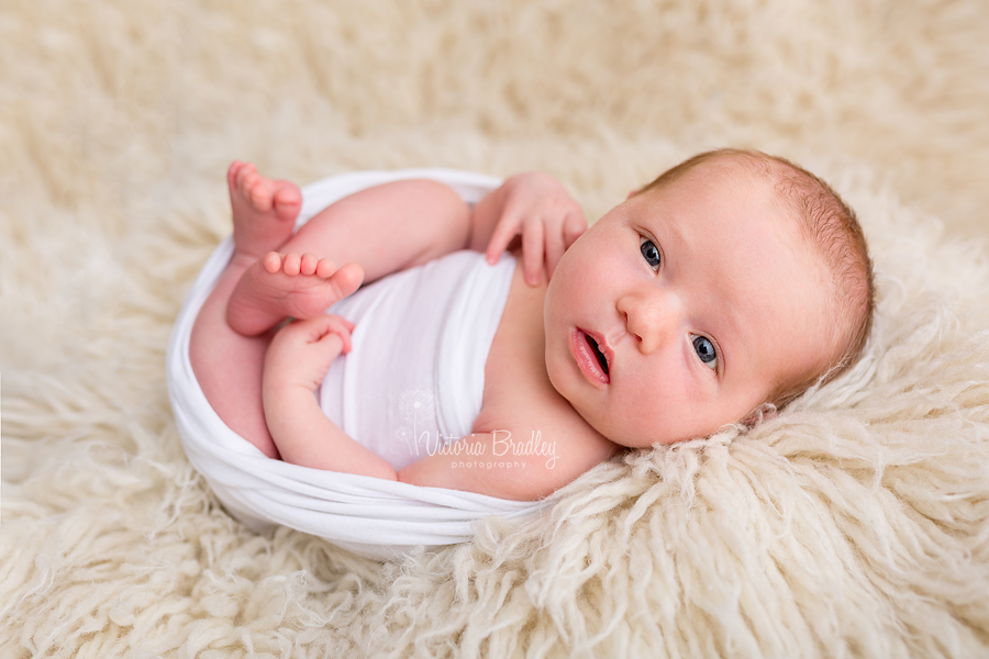 wrapped newborn baby girl in white wrap on a cream flokati.