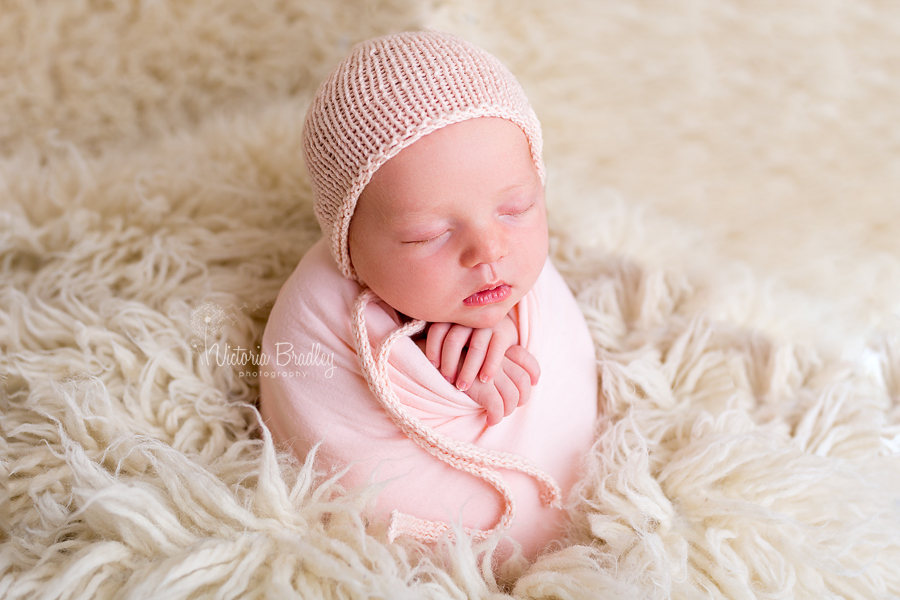 wrapped newborn baby girl in peach wrap on a cream flokati, potato sack pose newborn photography session