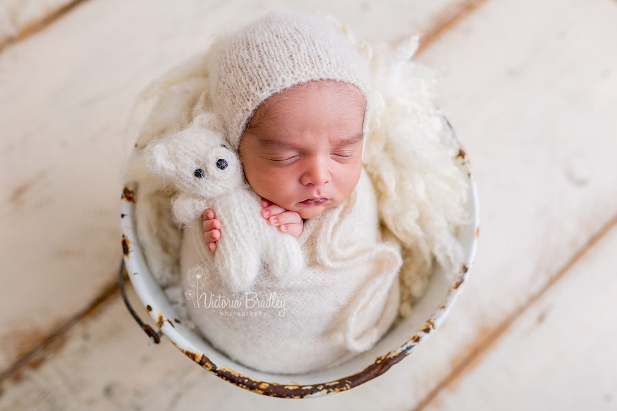 newborn holding tiny teddy in cream kitted wrap and bonnet