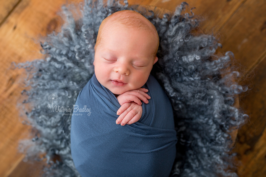 newborn baby boy photography session wrapped in blue on a blue felted curly layer