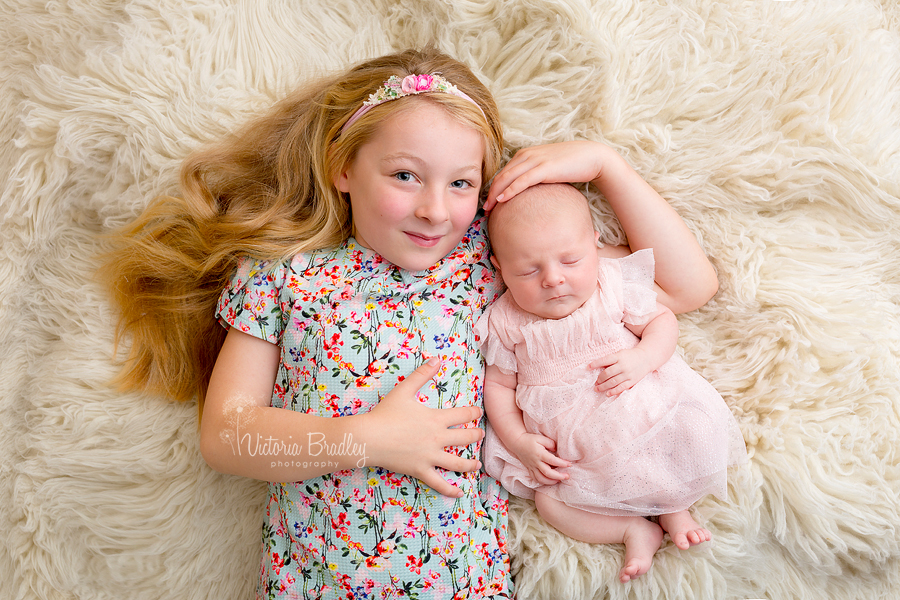 newborn baby girl photography with sibling on cream flokati in floral dress