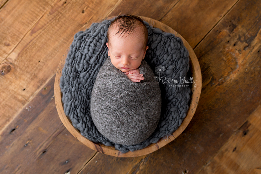 wrapped newborn baby boy photography session, grey wrap in a wooden bowl on wooden floor