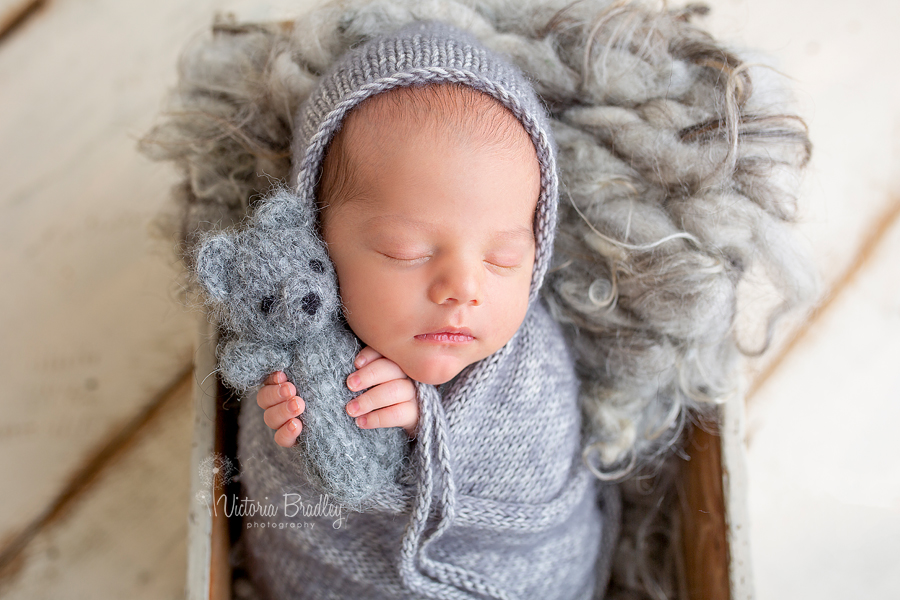 baby in white grey knitted wrap holding grey teddy