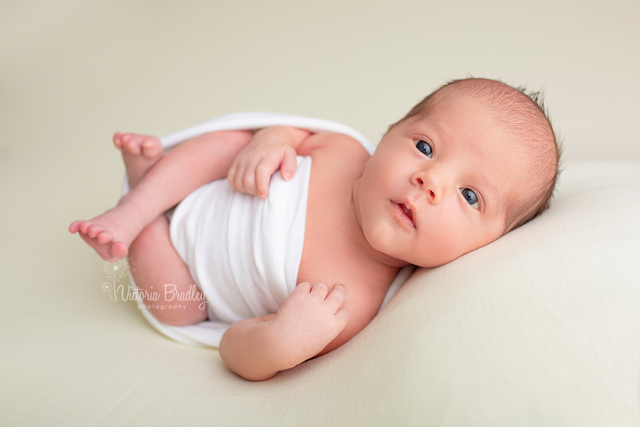 newborn photography session baby in white egg wrap on yellow backdrop