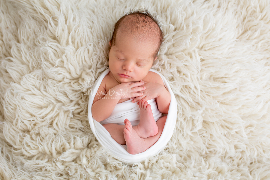 newborn photography session baby in white egg wrap on white flokati rug