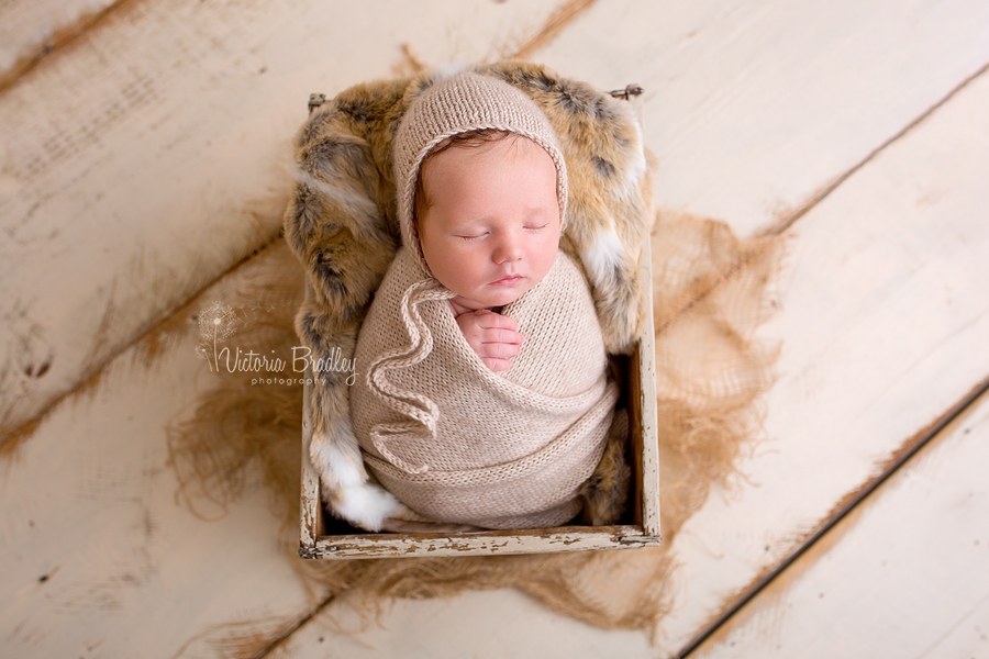 wrapped baby newborn in cream wrap with cream bonnet, in cream crate with fur, hessian and cream wooden painted floor