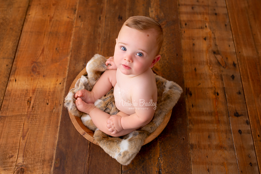 sitter baby boy in wooden bowl on wooden floor