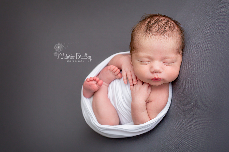 newborn wrapped baby on grey backdrop in white wrap