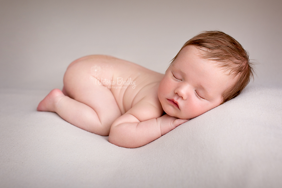 baby boy newborn on tummy on cream backdrop