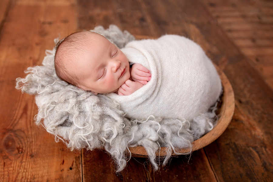 wrapped baby newborn on grey fur in wooden bowl