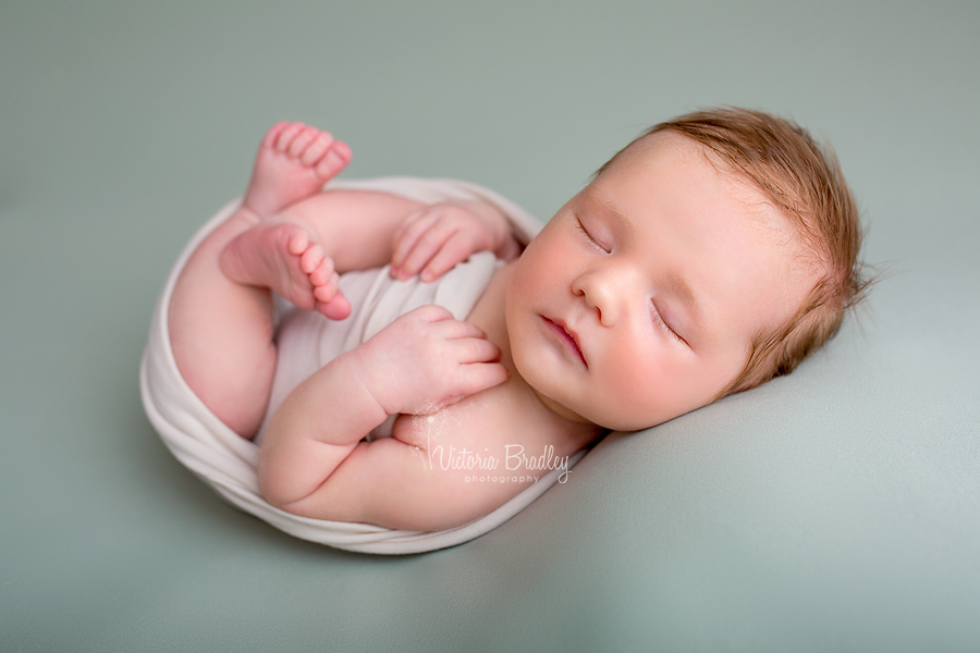 baby boy newborn on back on sage green newborn backdrop wrapped in cream wrap