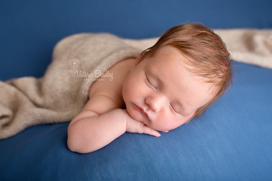 baby boy newborn on tummy on blue backdrop