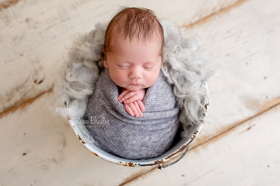 newborn wrapped baby in grey in a white bucket