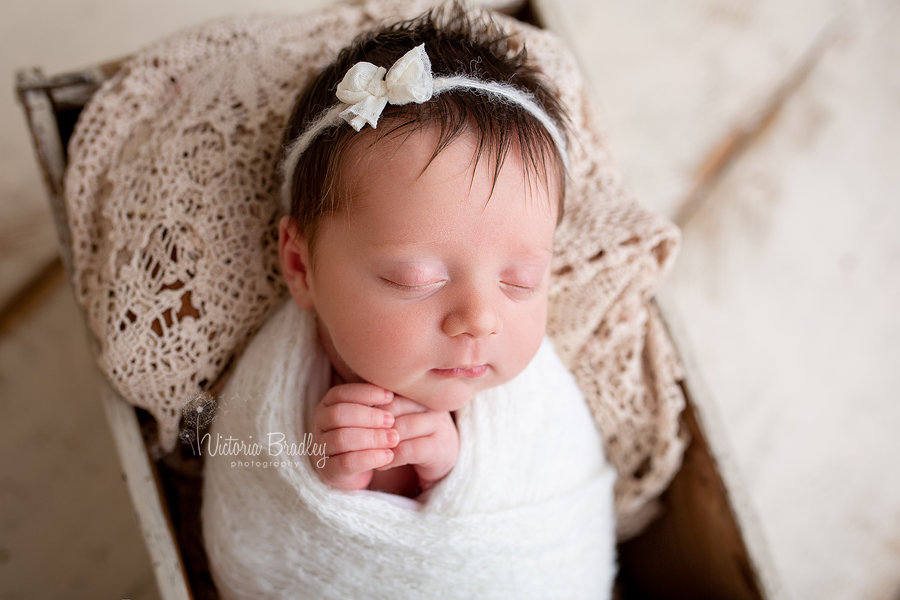 swaddled newborn baby girl in crate with vintage lace