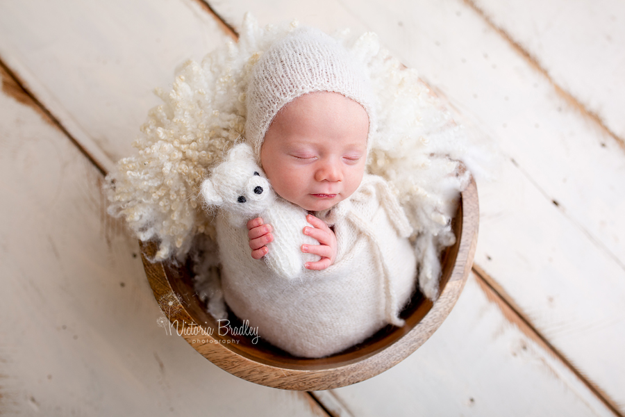 wrapped newborn baby boy with white teddy in wooden bowl