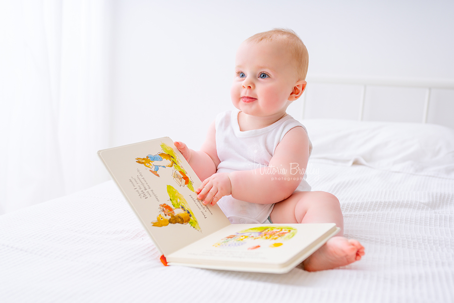 baby sitter boy reading book on white bed