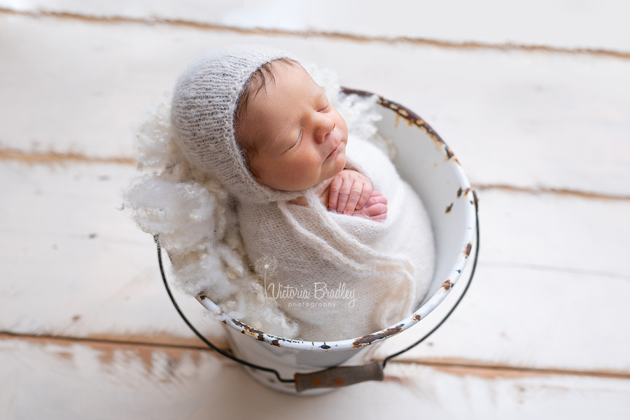 wrapped baby newborn session photography in metal bucket on cream wood floor