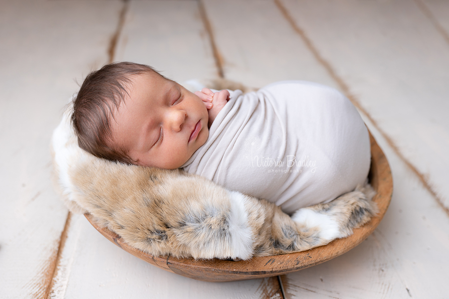 wrapped baby newborn session photography in wooden bowl on cream wood floor