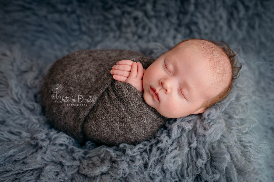 wrapped newborn photography in grey knitted wrap on grey flokati rug