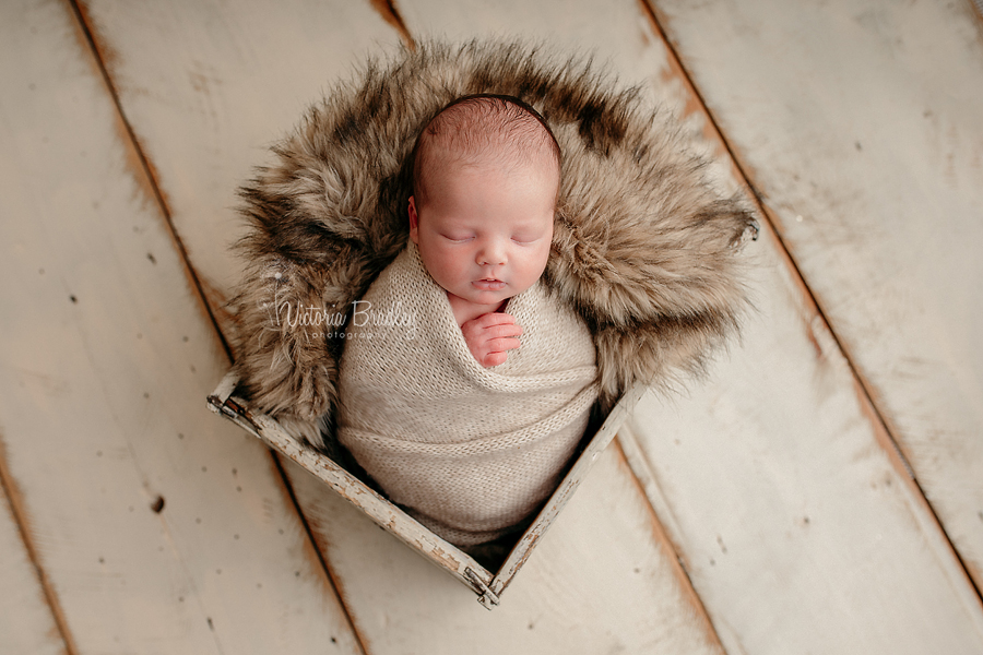 wrapped newborn baby photography, baby in crate, with fur, oatmeal wrap on cream wooden floor