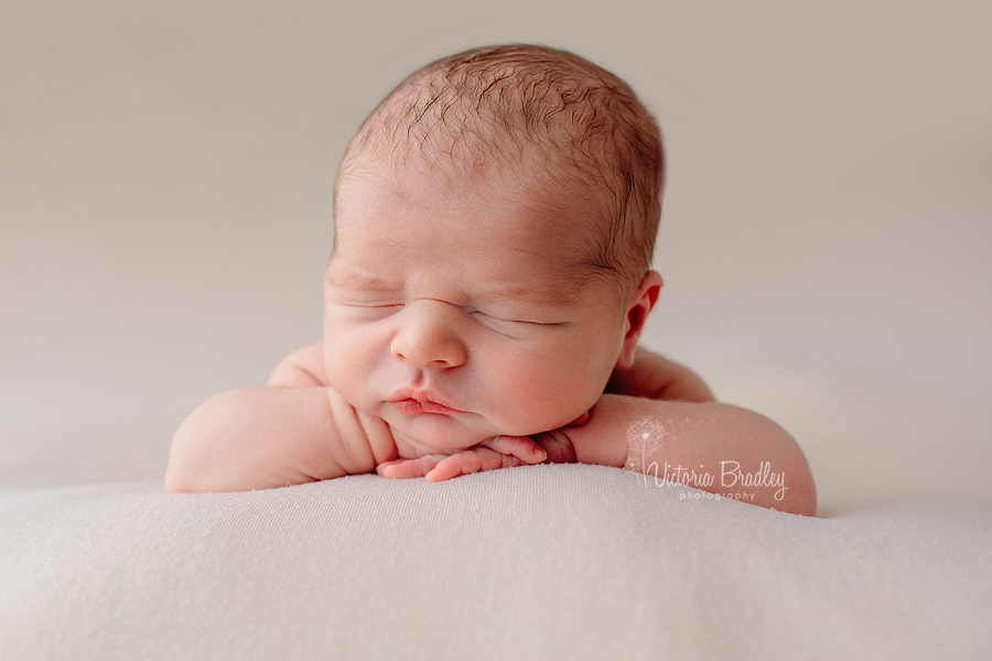 chin on hands pose baby newborn photo on cream backdrop