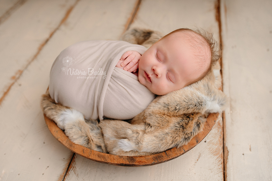 newborn baby boy wrapped on fur in wooden bowl