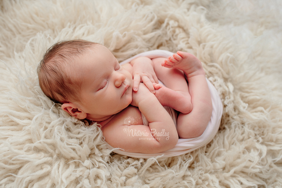 egg wrap newborn pose on cream flokati rug