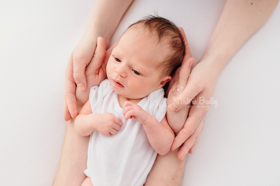 newborn baby on white with parents hands