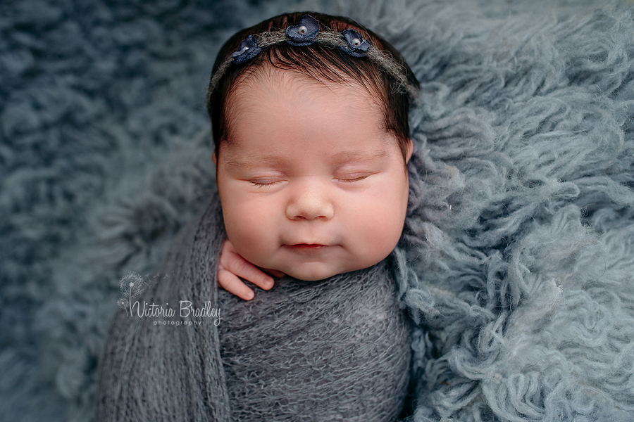 smiling newborn baby girl wrapped in grey