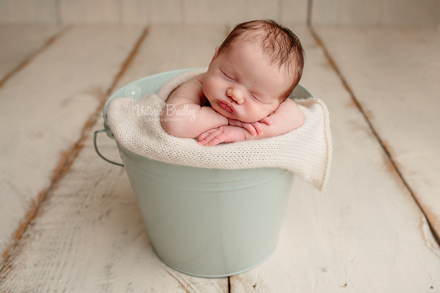 chin on hand pose newborn baby girl in mint bucket