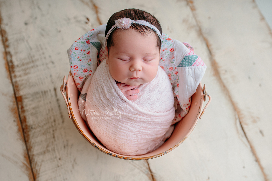 wrapped baby girl newborn in a pink bucket wrapped in a pink knit wrap