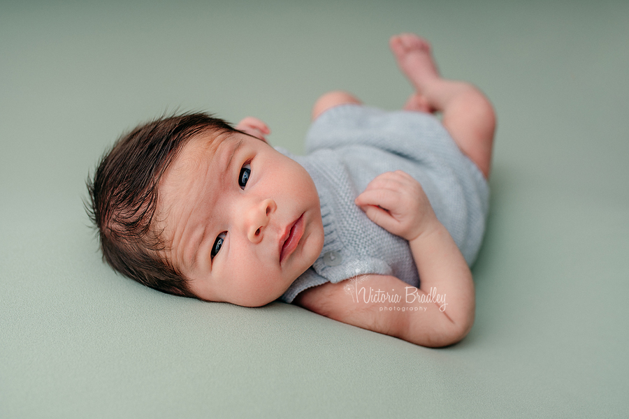 newborn on sage green backdrop with grey knitted outfit