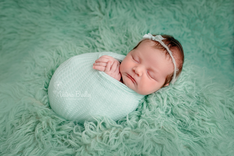 newborn on mint green flokati in mint green wrap