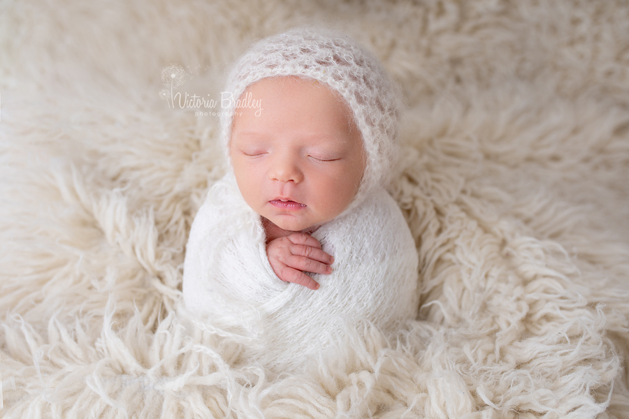 wrapped newborn potato sack pose with cream wrap and cream flokati