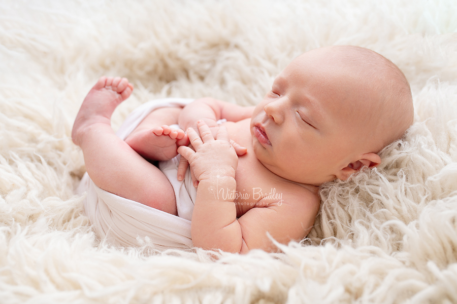 newborn baby egg wrap pose on cream flokati