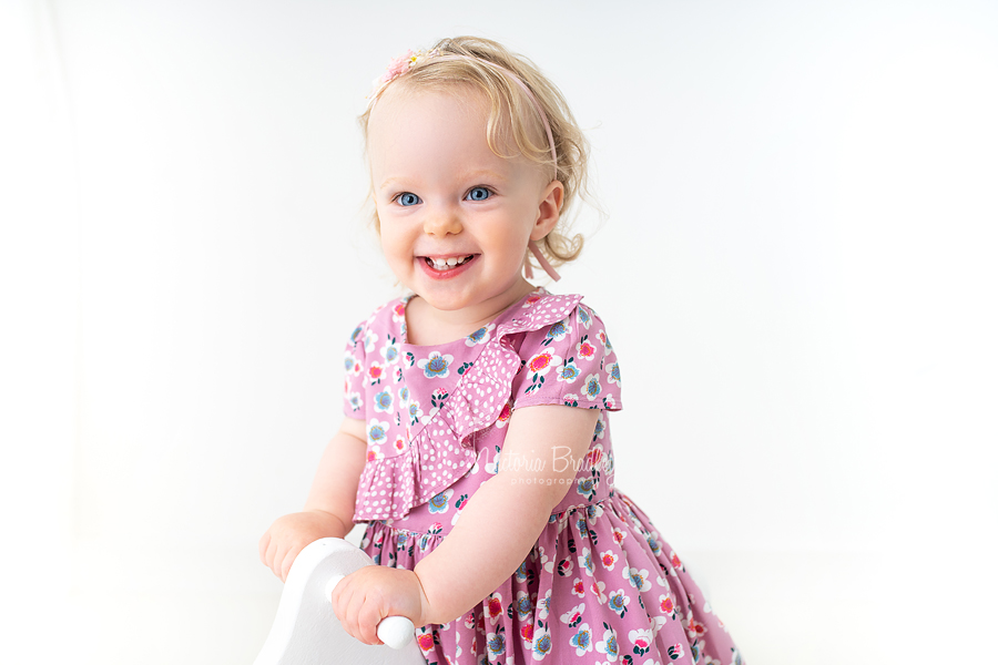 baby girl in floral dress on white rocking horse close up