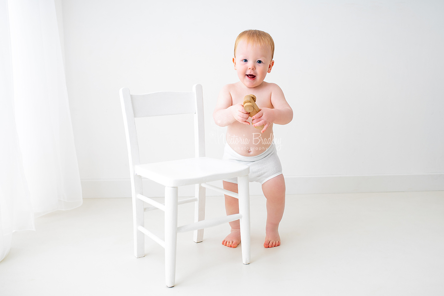 baby with wooden car next to white chair