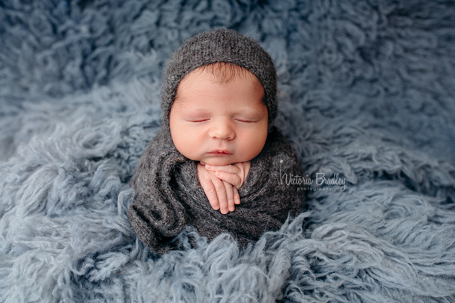 potato sack pose newborn on grey flokati with knitted grey wrap and bonnet