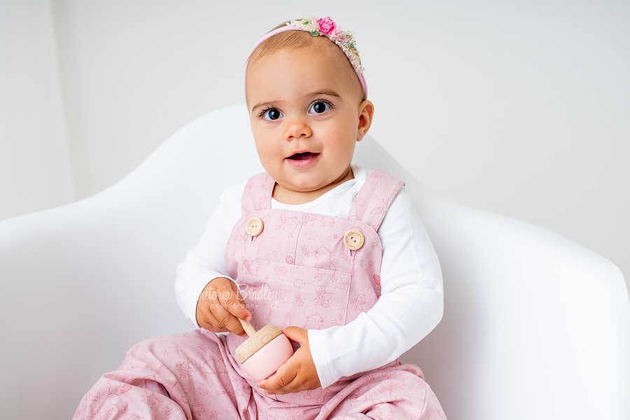 1 years old on white chair with pink dungarees 