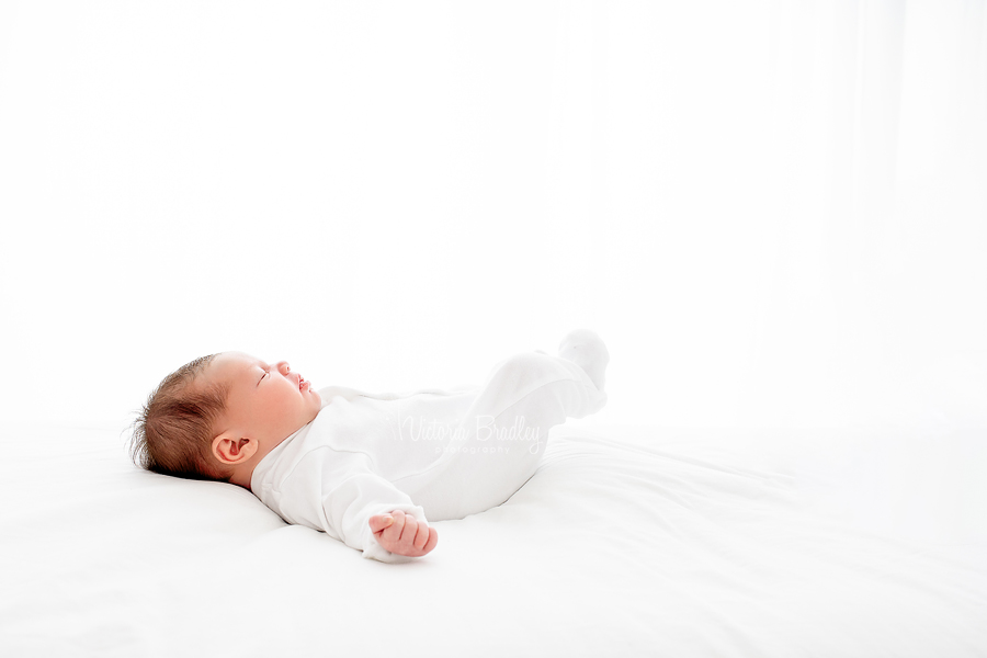 newborn in white romper on bed