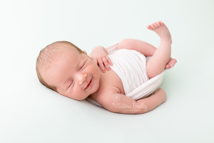 wrapped smiling newborn on mint backdrop