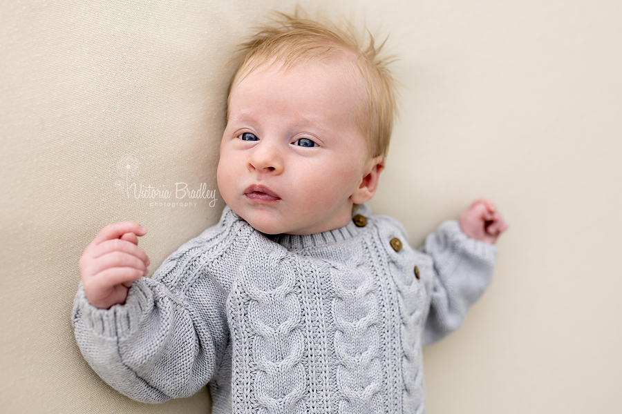 awake newborn boy in grey romper