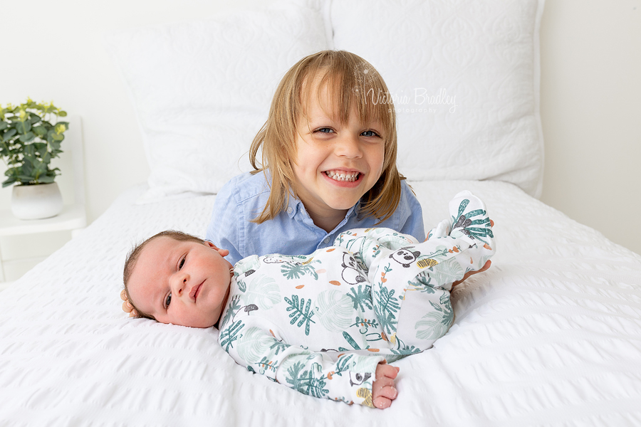 sibling and newborn on white bed