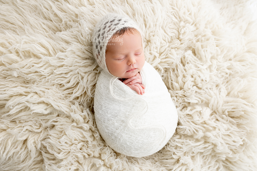 wrapped newborn on cream flokati