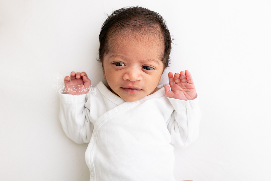 awake newborn baby on white backdrop with white top