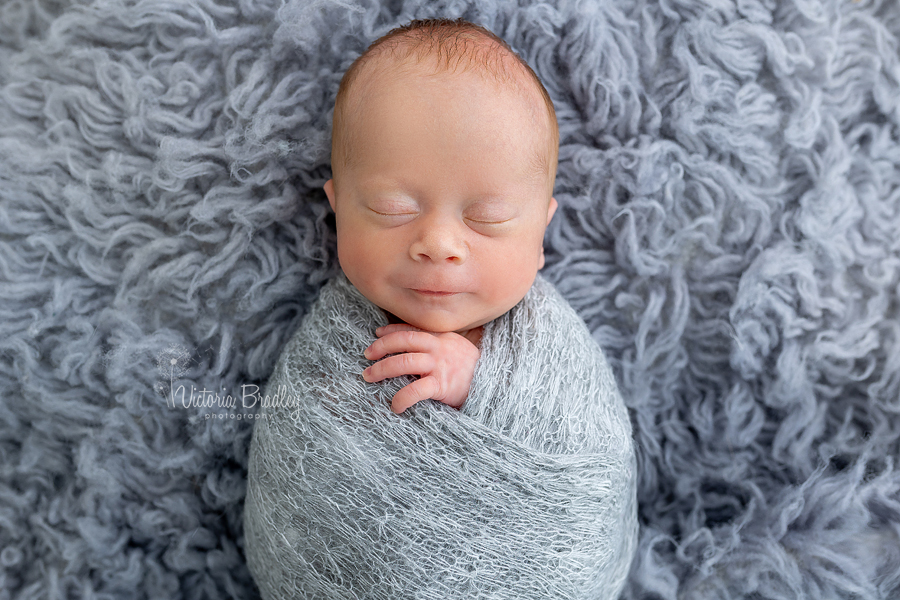 smiling wrapped newborn on grey