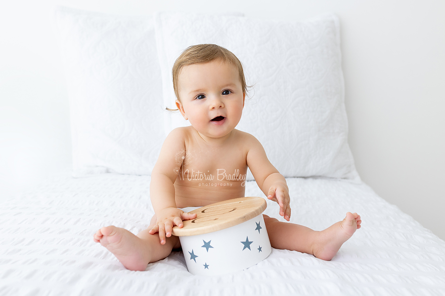 smiling baby boy on white bed with wooden drum